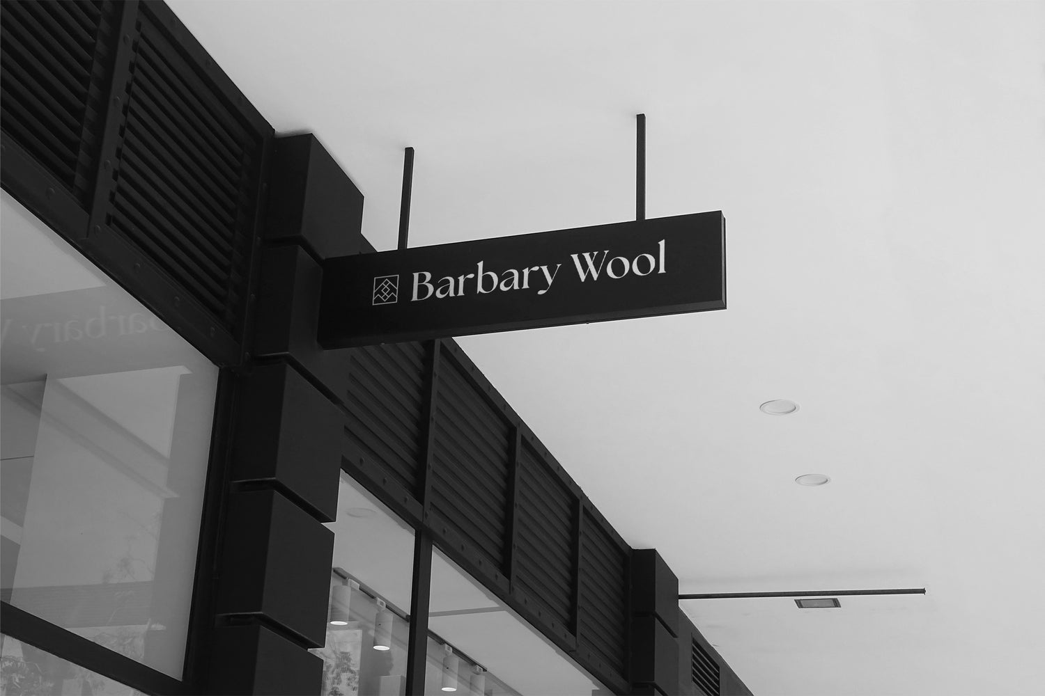 Storefront of Barbary Wool, showcasing a sleek black sign with the store name in elegant white font, positioned against a modern exterior with glass panels and minimalist architectural elements.