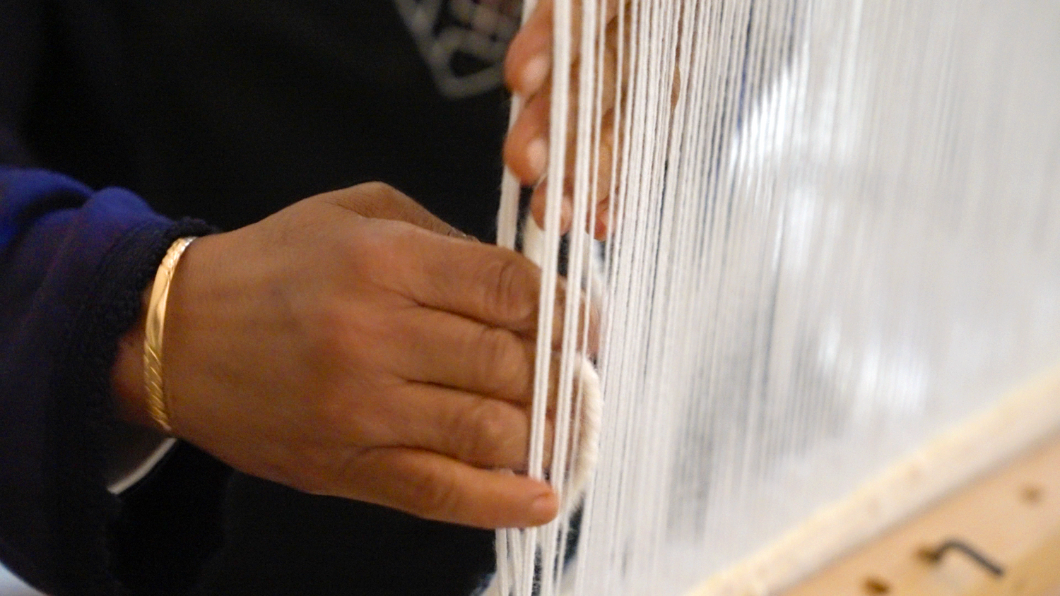 Close-up of skilled hands weaving wool threads on a loom, showcasing the craftsmanship behind Barbary Wool rugs.