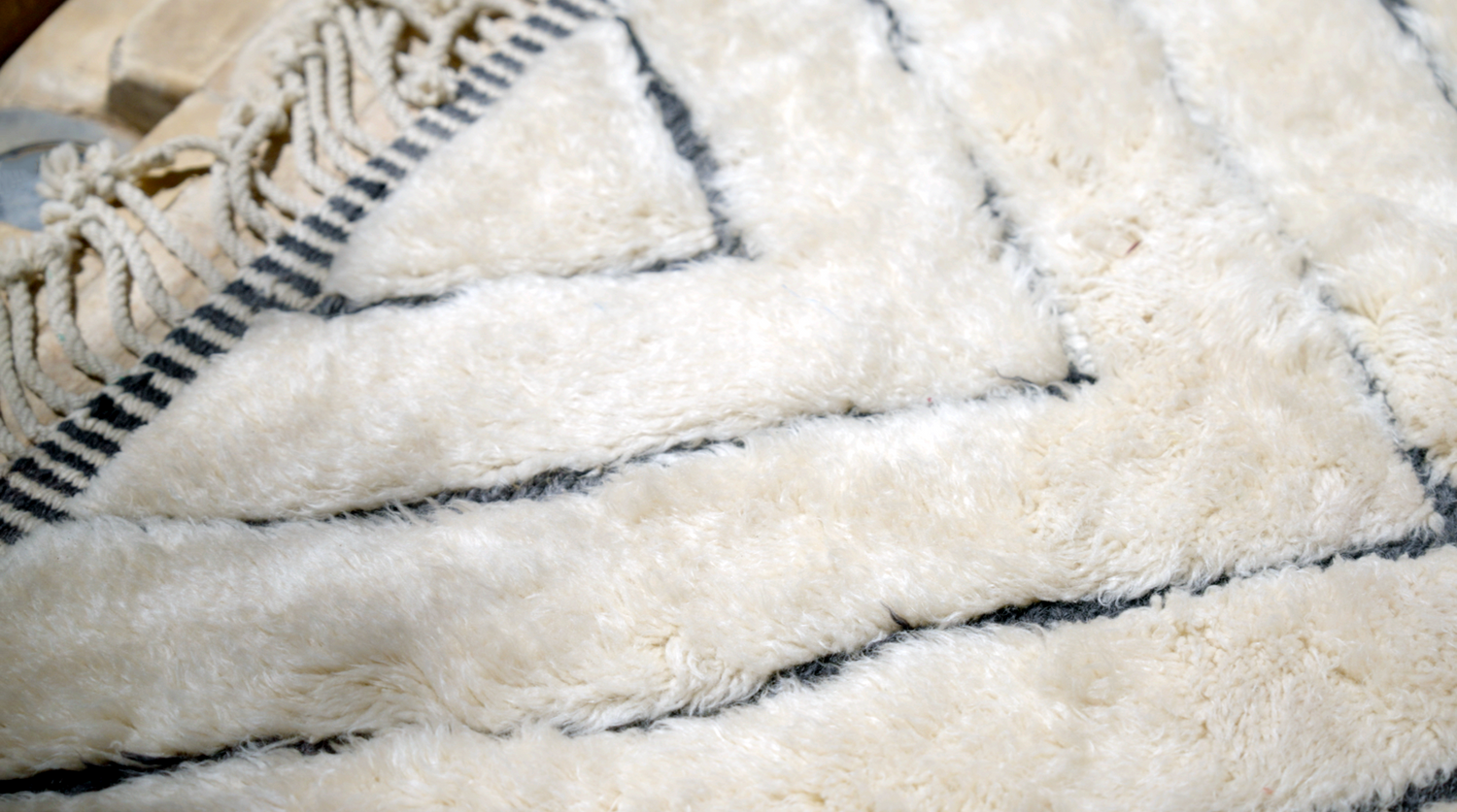 Close-up of a fluffy white wool rug with a geometric black pattern and fringe details, highlighting its soft texture.